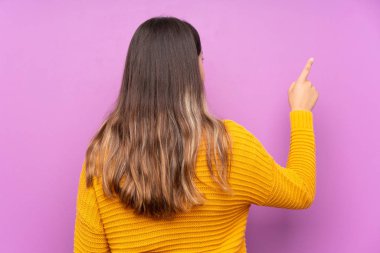 İzole edilmiş mor arka planda genç bir kadın işaret parmağıyla işaret ediyor.