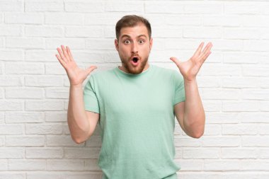 Sürpriz yüz ifadesi ile tuğla duvar üzerinde sarışın adam