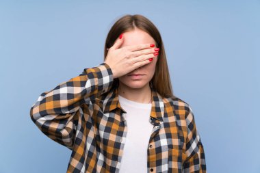 Elleri ile gözleri kaplayan mavi duvar üzerinde genç kadın