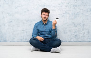 Yerde oturmuş elinde kredi kartı olan genç adam