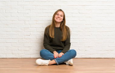 Genç bir kadın yerde oturmuş gülümsüyor.