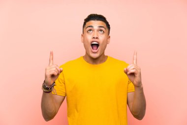 İşaret parmağı ile işaret izole pembe duvar üzerinde sarı gömlek ile genç adam harika bir fikir