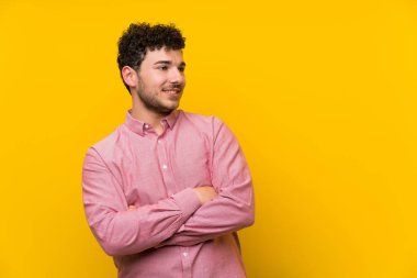 İzole sarı duvar ayakta ve yan bakarak üzerinde kıvırcık saçlı adam