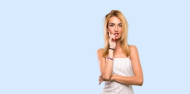 Genç sarışın kadın şaşırmış ve izole mavi arka plan üzerinde bakarken şok