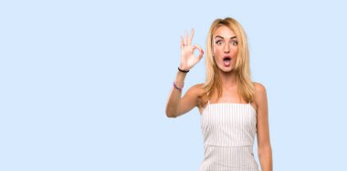 Genç sarışın kadın şaşırttı ve izole mavi arka plan üzerinde ok işareti gösteren