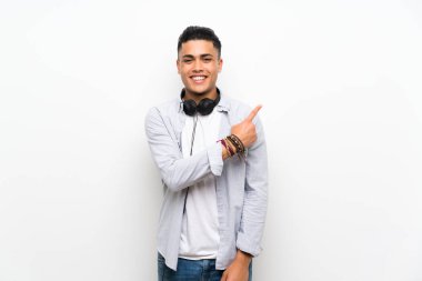 Bir ürün sunmak için yan işaret kulaklık ile izole beyaz duvar üzerinde genç adam