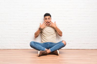 Genç bir adam yerde oturuyor ve yüzünde sürpriz bir ifade var.