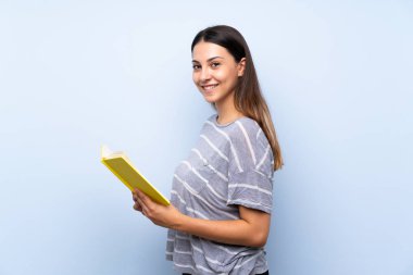 Izole mavi arka plan üzerinde genç esmer kadın tutma ve bir kitap okuma