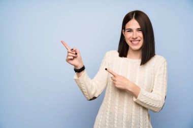 Izole mavi duvar üzerinde genç kadın yan parmak işaret