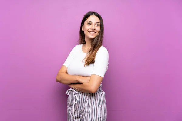 Young woman over isolated purple background with arms crossed and happy