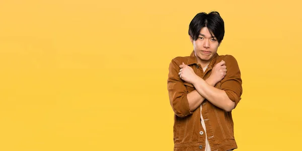 Asian man with brown jacket freezing over isolated yellow background