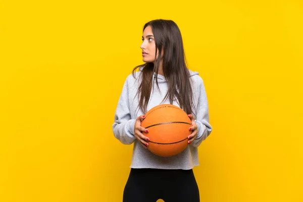 Wanita muda bermain basket melalui latar belakang kuning yang terisolasi — Stok Foto