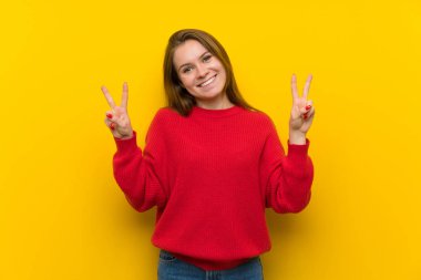 Sarı duvarın üzerinde iki eliyle zafer işareti gösteren genç kadın