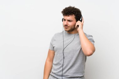 Izole duvar üzerinde kıvırcık saçlı adam kulaklık ile müzik dinlerken