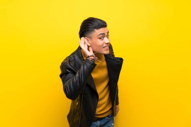 Izole sarı arka plan üzerinde genç adam kulak elini koyarak bir şey dinlerken