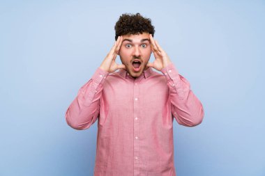 Sürpriz ifade ile izole mavi duvar üzerinde kıvırcık saçlı Adam