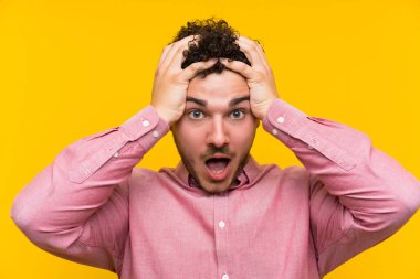 Sürpriz yüz ifadesi ile izole sarı duvar üzerinde kıvırcık saçlı Adam