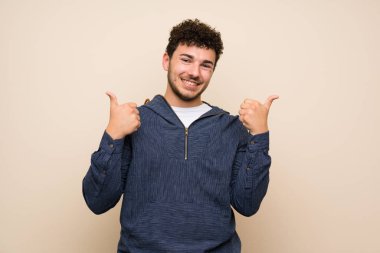 Jest kadar başparmak ve gülümseyerek izole duvar üzerinde kıvırcık saçlı adam