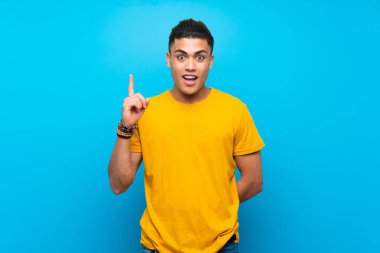 Izole mavi arka plan üzerinde sarı gömlekli genç adam bir fikir parmağını işaret düşünme