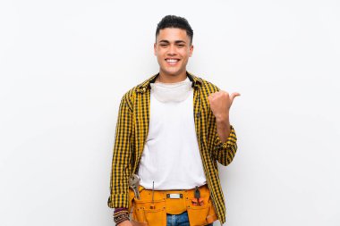 Izole beyaz duvar üzerinde genç elektrikçi adam bir ürün sunmak için yan işaret