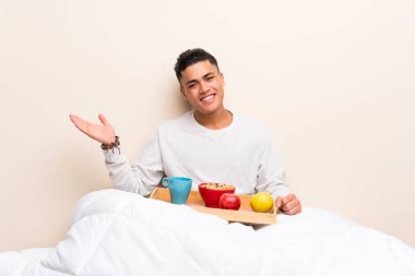 Genç adam avuç içinde taklit alanı hayali tutarak yatakta kahvaltı yapıyor