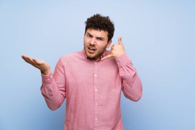 Izole mavi duvar üzerinde kıvırcık saçlı adam telefon jest yapma ve şüphe