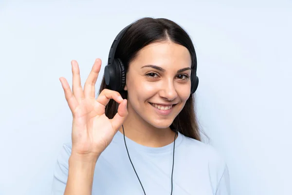 Mujer Joven Escuchando Música Sobre Fondo Azul Aislado Mostrando Signo —  Fotos de Stock