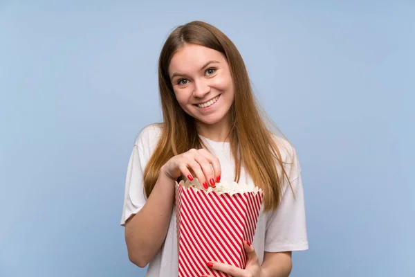 Młoda Kobieta Nad Niebieską Ścianą Zaskoczony Jedzenie Popcorns — Zdjęcie stockowe