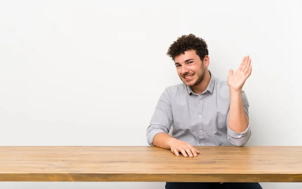 Jovem Com Uma Mesa Saudando Com Mão Com Expressão Feliz — Fotografia de Stock