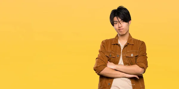 Asian man with brown jacket feeling upset over isolated yellow background