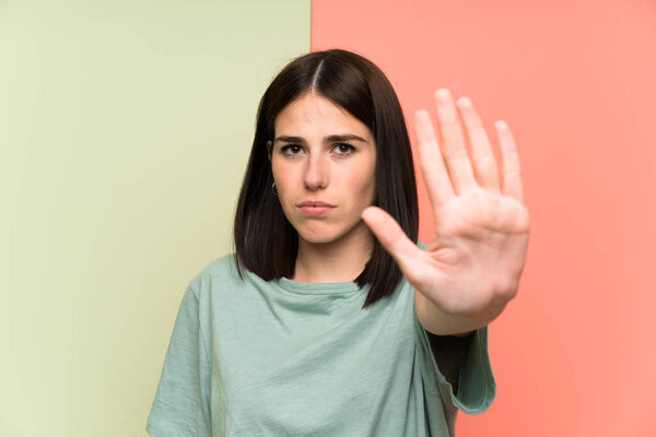 Young woman over isolated colorful wall making stop gesture with her hand