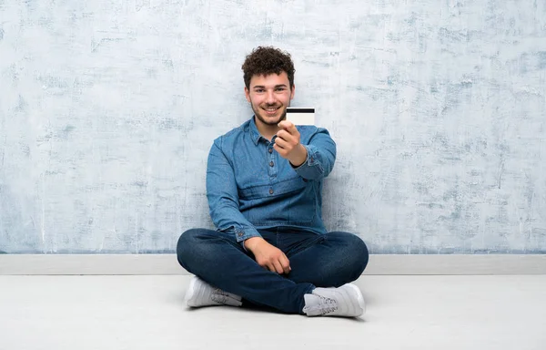 Junger Mann Sitzt Auf Dem Boden Und Hält Eine Kreditkarte — Stockfoto