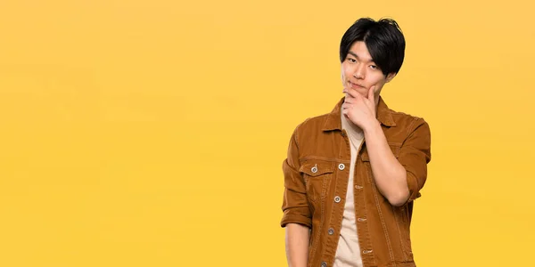 Asian Man Brown Jacket Thinking Isolated Yellow Background — Stock Photo, Image