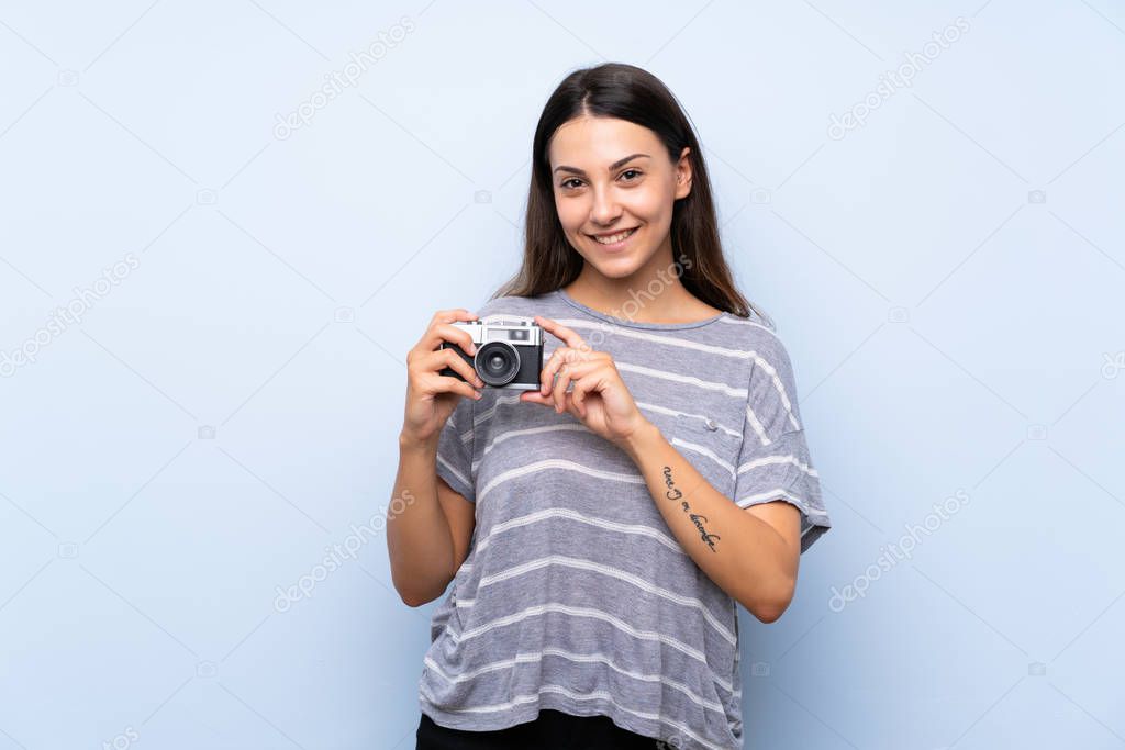 Young brunette woman over isolated blue background holding a camera