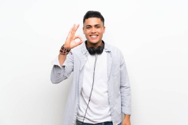 Parmakları ile ok işareti gösteren kulaklıkile izole beyaz duvar üzerinde genç adam