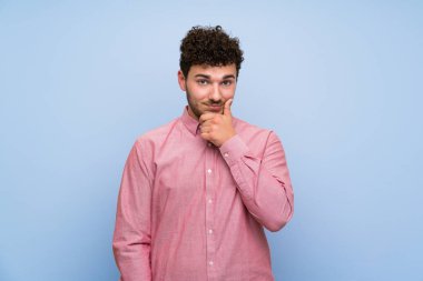 İzole mavi duvar düşünme üzerinde kıvırcık saçlı adam