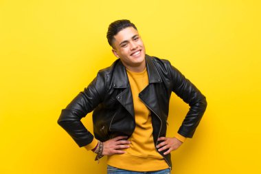 Izole sarı arka plan üzerinde genç adam kalça kolları ile poz ve gülümseyerek