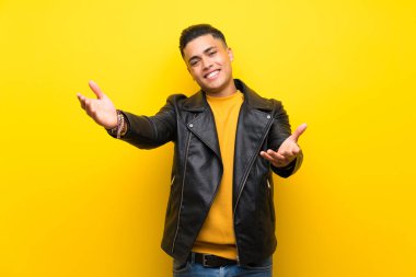 Izole sarı arka plan üzerinde genç adam sunan ve el ile gelmek için davet