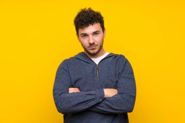 Kollarını çapraz tutan izole sarı duvar üzerinde genç adam