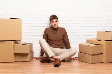 Yakışıklı genç adam kutuları arasında yeni bir evde hareket ayakta ve yan bakıyor