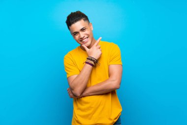 Izole mavi arka plan üzerinde sarı gömlekli genç adam gülümseyerek