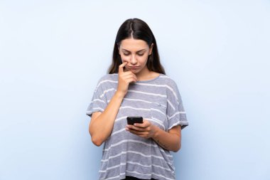 Cep telefonu kullanarak izole mavi arka plan üzerinde genç esmer kadın