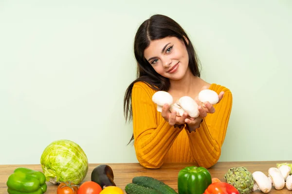 Happy Teenager girl with many vegetables over green wall