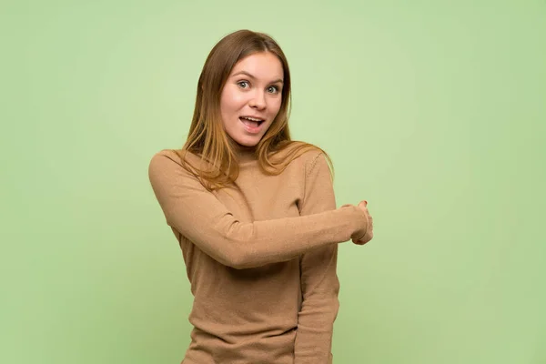 タートルネックのセーターを持つ若い女性が後ろを指差す — ストック写真