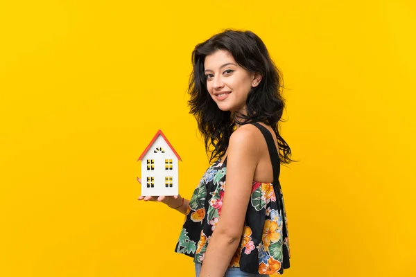 小さな家を持つ孤立した黄色の背景の上の若い女性 — ストック写真