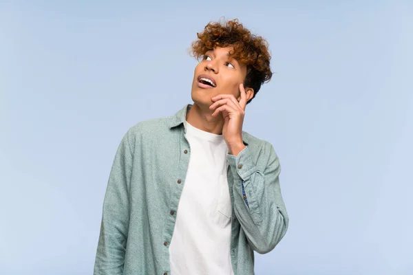 Joven Afroamericano Sobre Aislado Muro Azul Pensando Una Idea Mientras —  Fotos de Stock