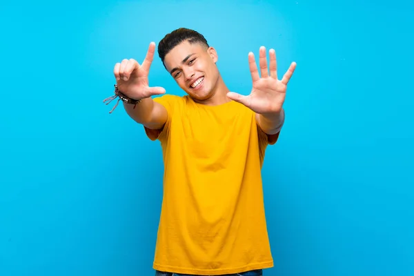 Young man with yellow shirt over isolated blue background counting seven with fingers