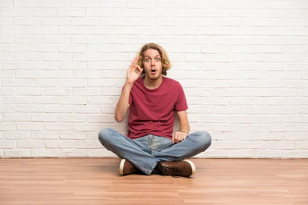 Blonde Man Zittend Vloer Verrast Toont Teken — Stockfoto