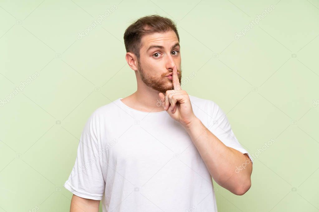 Handsome man over green background doing silence gesture