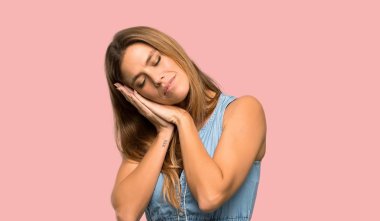 İzole pembe arka plan üzerinde dorable ifade uyku jest yapma jean elbiseile Sarışın kadın